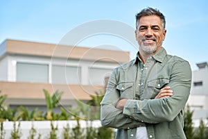 Happy mature man new property owner or realtor standing outside country house.