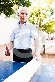 Happy mature man posing with rackets at table tennis