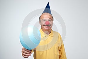 Happy mature man with red clown nose and blue ballon on birthday party.