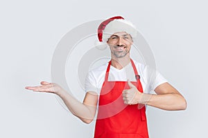 happy mature man in red waiter apron and christmas santa hat. thumb up