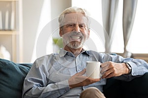 Happy mature man resting on sofa with coffee in hands.