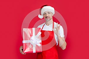 happy mature man in santa claus hat and red apron hold present