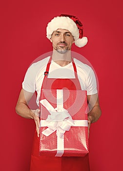 happy mature man in santa hat and red apron hold box
