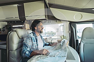 Happy mature man smilng inside a camper camping car using paper map guide to plan destinations holiday. Vanlife lifestyle