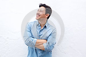 Happy mature man standing with arms crossed against white wall and looking away
