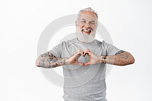 Happy mature man with tattoos laughing, showing heart I love you gesture, express sympathy, like or care for someone