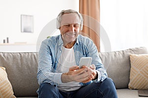 Happy mature man using cellphone wearing headphones