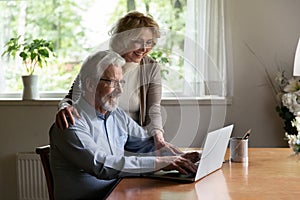 Happy mature man and woman using laptop together, chatting online
