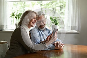 Happy mature man and woman using phone together, browsing apps