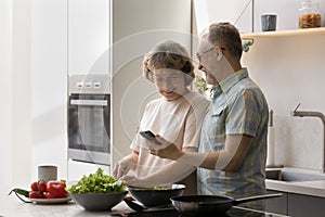 Happy mature married couple cooking in home kitchen