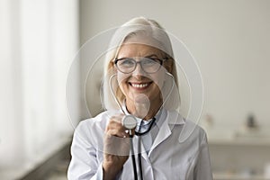 Happy mature medical practitioner using stethoscope head shot portrait