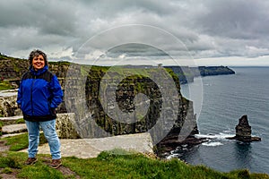 Happy mature Mexican woman on the Cliffs of Moher and the Branaunmore sea stack in the background