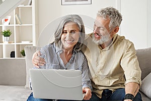 Happy mature mid age couple doing ecommerce shopping using laptop at home.