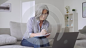 Happy mature mid age woman working using laptop computer from home office.