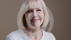 Happy mature middle-aged blonde smiling caucasian 60s woman looking at camera posing in studio portrait, cheerful older