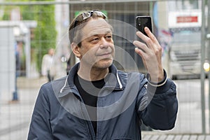 A happy mature middle-aged man using a mobile phone is sitting outside.