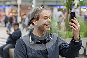 A happy mature middle-aged man using a mobile phone is sitting outside.