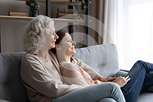 Happy mature mom and adult daughter relax on sofa dreaming