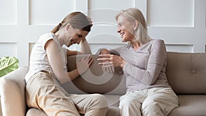 Happy mature mom and grownup daughter talk on couch