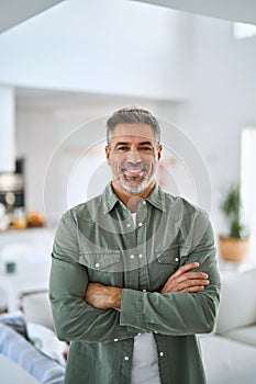 Happy mature older man standing with arms crossed at home. Vertical portrait.