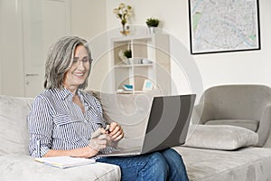 Happy mature mid age woman working on laptop computer from home office.