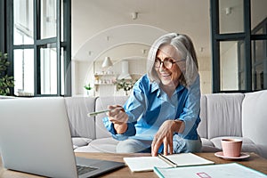 Happy mature older woman video calling on laptop working from home. photo