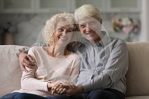 Happy mature retired husband and wife hugging on home couch