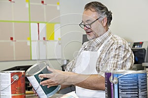 Happy mature sales clerk reading instructions paint can in hardware store