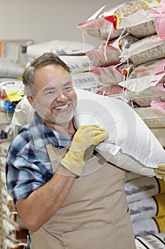 Happy mature salesperson carrying sack in feed store