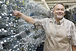 Happy mature salesperson holding metallic equipment while looking away in hardware store