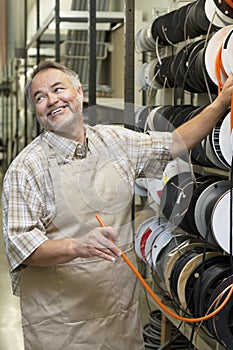 Happy mature salesperson standing by electrical wire spool while looking away in hardware store
