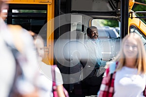 happy mature school bus driver looking at teenagers walking