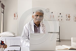 Happy mature senior Indian doctor man sitting at clinic workplace