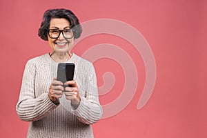Happy mature senior woman holding smartphone using mobile online apps, smiling old middle aged grandmother texting sms message