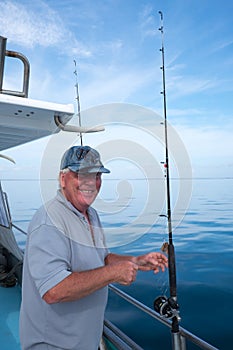 Happy mature smiling tourist on fishing boat charter with rod in