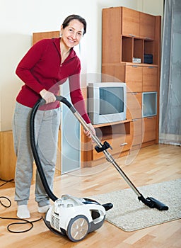 Happy mature woman cleaning with vacuum cleaner