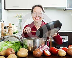 Happy mature woman cooking with skillet