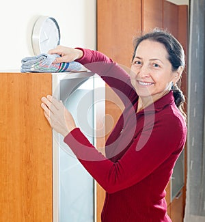 Happy mature woman dusting furniture