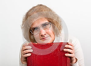 Happy mature woman with glasses holding old red paperback book Bible