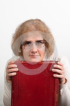 Happy mature woman with glasses holding old red paperback book Bible