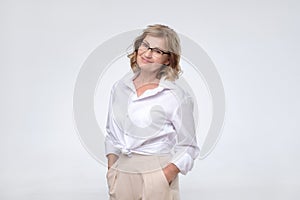 Happy mature woman in glasses and white shirt standing on a white background.