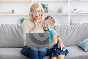 Happy mature woman and granddaughter using laptop