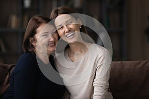 Happy mature woman with grownup daughter hugging sitting on couch