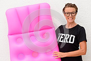 Happy mature woman holding air mattress and standing against white background outdoors