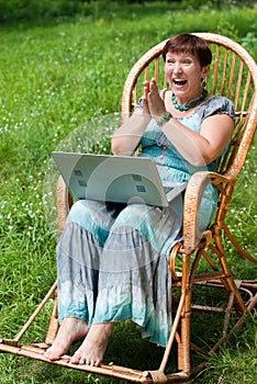 Happy mature woman with laptop in rocking chair
