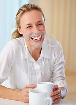 Happy mature woman, laughing and coffee for funny joke, conversation or humor on kitchen table at home. Blonde female