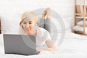 Happy mature woman laying in bed and watching movie