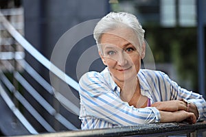 Happy mature woman near metal handrail on street, space for text. Smart aging