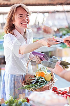 Happy mature woman paying for fresh organic vegetables in a local marketplace