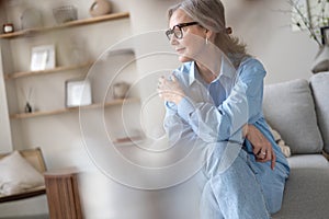 Happy mature woman relaxing on her couch at home in the living room. Portrait of happy woman in blue shirt smiling